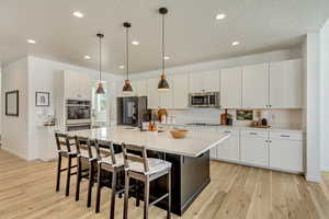 Kitchen with a sink, an island with sink, light wood-style floors, stainless steel appliances, and light countertops