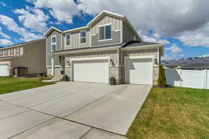 View of front of property featuring board and batten siding, stone siding, concrete driveway, and fence
