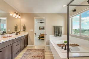 Bathroom featuring wood finished floors, ensuite bathroom, a sink, a bath, and double vanity