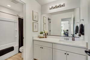 Bathroom featuring toilet, visible vents, shower / bath combo with shower curtain, wood finished floors, and vanity