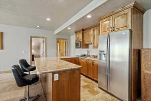 Kitchen with stainless steel appliances, a sink, recessed lighting, light stone counters, and a breakfast bar
