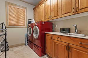 Washroom with cabinet space, independent washer and dryer, baseboards, and a sink