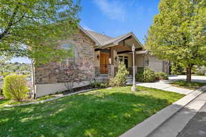 View of front of home with an attached garage, driveway, stone siding, and a front lawn