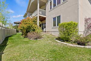 View of side of home featuring fence, a balcony, a yard, and stucco siding