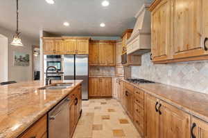 Kitchen with recessed lighting, a sink, premium range hood, light stone countertops, and appliances with stainless steel finishes