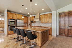 Kitchen with a sink, stainless steel appliances, custom range hood, light stone countertops, and recessed lighting