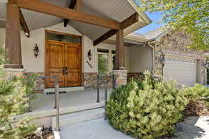 Property entrance with stucco siding, an attached garage, stone siding, and covered porch
