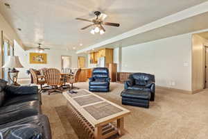 Living room featuring visible vents, a ceiling fan, baseboards, and light carpet