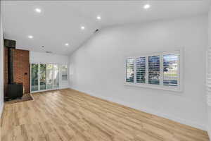 Unfurnished living room featuring light wood finished floors, visible vents, baseboards, high vaulted ceiling, and a wood stove