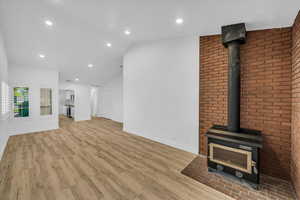 Unfurnished living room with light wood finished floors, vaulted ceiling, baseboards, recessed lighting, and a wood stove