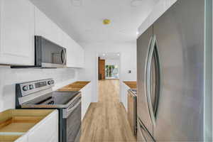 Kitchen with white cabinets, stainless steel appliances, and light wood-style floors