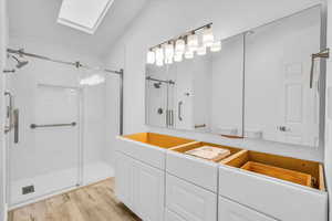 Bathroom with a shower stall, vaulted ceiling with skylight, wood finished floors, vanity, and toilet