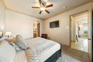 Bedroom with baseboards, arched walkways, light colored carpet, and crown molding