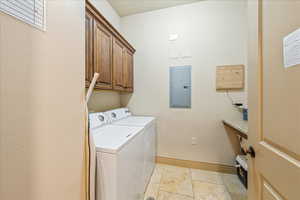 Laundry area featuring electric panel, stone tile flooring, cabinet space, washing machine and dryer, and baseboards