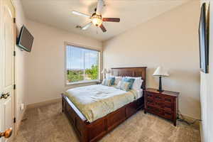 Bedroom with baseboards, visible vents, light colored carpet, and ceiling fan