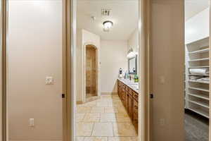 Full bathroom with stone tile flooring, a textured ceiling, double vanity, visible vents, and a shower stall