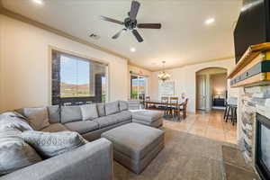 Living area featuring crown molding, a stone fireplace, ceiling fan with notable chandelier, arched walkways, and visible vents