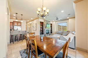 Dining area featuring visible vents, recessed lighting, ceiling fan with notable chandelier, crown molding, and a stone fireplace