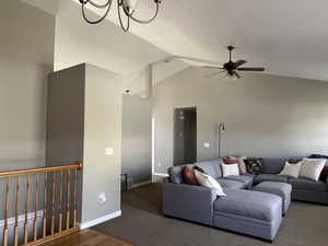 Living room featuring ceiling fan with notable chandelier, baseboards, wood finished floors, and high vaulted ceiling