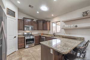 Kitchen featuring lofted ceiling, a kitchen breakfast bar, a sink, a peninsula, and appliances with stainless steel finishes