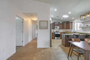 Kitchen featuring vaulted ceiling, light tile patterned floors, a peninsula, appliances with stainless steel finishes, and visible vents