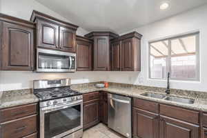 Kitchen featuring light stone counters, dark brown cabinets, a sink, light tile patterned flooring, and stainless steel appliances