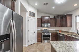 Kitchen with light stone counters, stainless steel appliances, vaulted ceiling, visible vents, and a sink