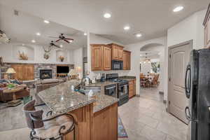 Kitchen featuring a sink, dark stone counters, black appliances, a peninsula, and ceiling fan