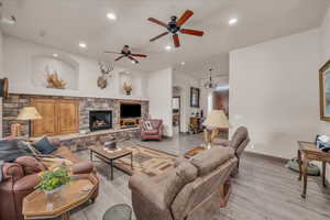 Living area featuring light wood-style flooring, ceiling fan, a fireplace, baseboards, and recessed lighting
