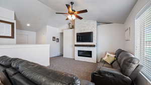 Carpeted living area featuring vaulted ceiling, baseboards, visible vents, ceiling fan, and a stone fireplace