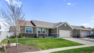Craftsman house with stone siding, board and batten siding, an attached garage, fence, and a front yard