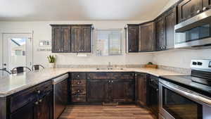 Kitchen with dark brown cabinets, appliances with stainless steel finishes, dark wood-style flooring, and a sink