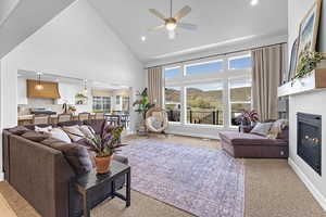 Living room with high vaulted ceiling, light carpet, a glass covered fireplace, and recessed lighting