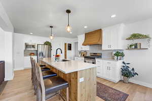 Kitchen with light wood-style flooring, stainless steel appliances, a sink, and custom range hood