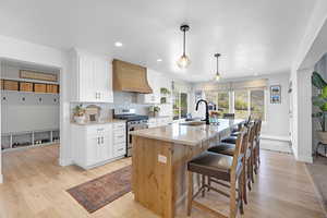 Kitchen featuring light countertops, a sink, double oven range, a kitchen island with sink, and custom range hood