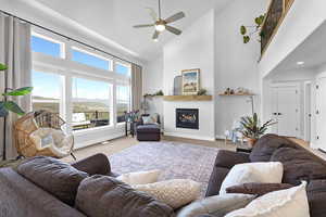 Living area featuring high vaulted ceiling, a ceiling fan, a glass covered fireplace, carpet floors, and baseboards