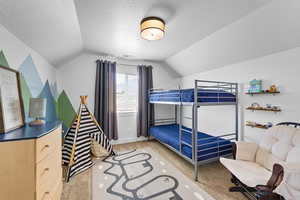 Bedroom with lofted ceiling, a textured ceiling, and light colored carpet
