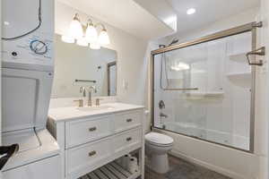 Full bathroom featuring wood finished floors, vanity, stacked washer / drying machine, enclosed tub / shower combo, and toilet