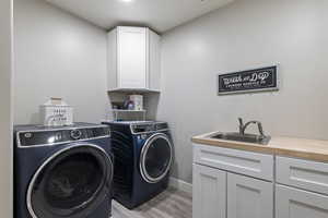 Clothes washing area with washing machine and clothes dryer, light wood-style flooring, a sink, baseboards, and cabinet space