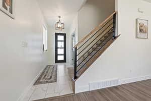 Entrance foyer with baseboards, visible vents, an inviting chandelier, marble finish floor, and stairway