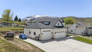 View of side of home with concrete driveway, an attached garage, stone siding, roof with shingles, and a mountain view