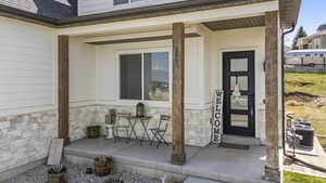 Property entrance featuring central AC unit, a porch, stone siding, and a shingled roof