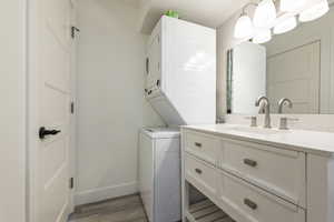 Clothes washing area with stacked washer / drying machine, laundry area, a sink, light wood-style floors, and baseboards