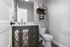 Half bath featuring baseboards, wood finished floors, toilet, and vanity
