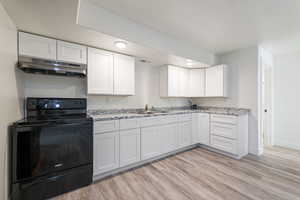 Kitchen featuring light wood-type flooring, black range with electric stovetop, under cabinet range hood, and a sink