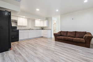 Kitchen featuring white cabinets, open floor plan, light stone counters, under cabinet range hood, and black appliances