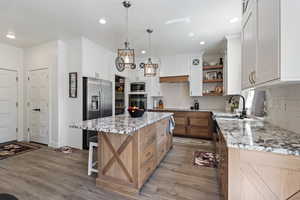 Kitchen with open shelves, a sink, light wood-style floors, appliances with stainless steel finishes, and a kitchen island