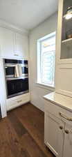 Kitchen featuring a textured ceiling, light stone countertops, double oven, dark wood-style floors, and white cabinetry