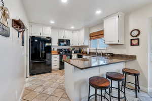 Kitchen featuring dark stone countertops, white cabinetry, a sink, black appliances, and a peninsula