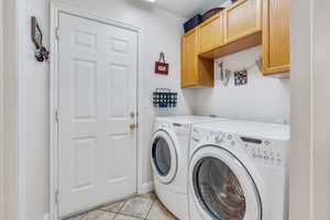 Laundry area with light tile patterned floors, washing machine and clothes dryer, and cabinet space